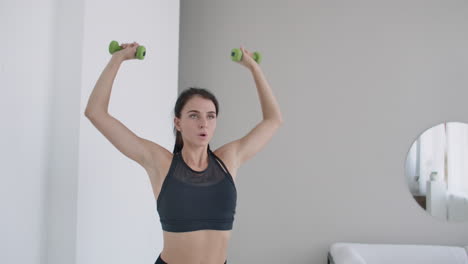 Raise-the-dumbbells-over-your-head-performing-exercises-for-the-shoulders.-Training-at-home-in-the-apartment.-A-brunette-woman-with-long-hair-and-a-beautiful-figure